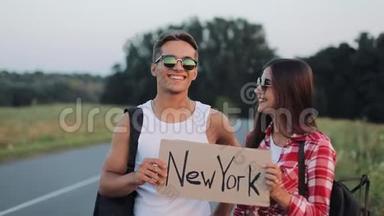 年轻的旅行情侣相爱，站在路上，举着纽约的标志。 快乐的微笑的朋友们正在注视